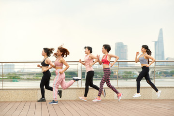 Obraz premium Side view of modern ethnic women in team jogging together on waterfront of city
