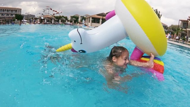 Little happy girl and her mom floating on an inflatable unicorn in the pool, having fun together.