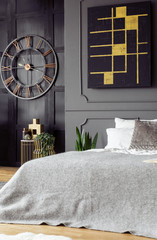Real photo of bed with bright bedclothes in bedroom interior with black and gold painting, fresh...