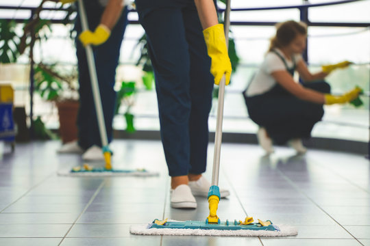 Close-up on person with yellow gloves holding mop while cleaning the floor