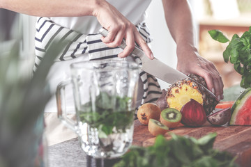 Jar of water with mint next to a woman cutting a pineapple