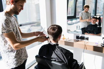 Barber in Barbershop cutting a client's hair with an electric razor for fashionable hairstyle.