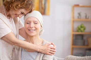 Smiling redhead woman hugging her sick sister who is suffering from lung cancer