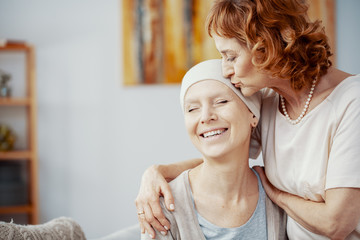 Senior redhead woman kissing forehead of her happy best friend suffering from cervical cancer - obrazy, fototapety, plakaty