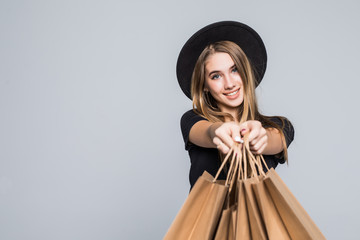 Portrait fashionable attractive happy woman in floppy hat, sunglasses holding packages bags with purchases after shopping pointed on you isolated on gray background. Copy space for advertisement