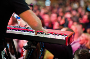 Artist play on audio piano on stage in a concert hall behing peoples.