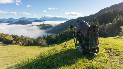 Fototapeta na wymiar man on wheelchair taking photos of beautiful landscape in a foggy morning, St. Thomas Slovenia