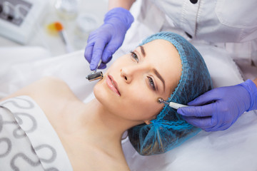 Cosmetology. Beautiful Woman At Spa Clinic Receiving Stimulating Electric Facial Treatment From Therapist. Closeup Of Young Female Face During Microcurrent Therapy.