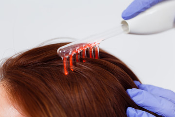 Fototapeta premium A young woman visited a dermatologist. Receiving electric darsonval facial massage procedure at beauty salon. White background