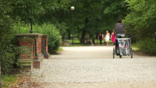 Unrecognizable man rides a bike on a park path. A children's wheel is attached to the back. Children's mode of transport