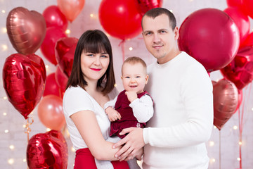 valentine's day concept - young family with daughter over red heart-shaped balloons background