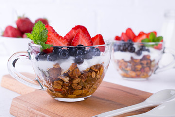Homemade Greek yogurt with granola, mint, blueberries and strawberry in a glass cups on white background, Health breakfast  concept