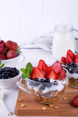 Healthy breakfast in a cup with homemade baked granola, fresh berries, and yogurt on a white table background