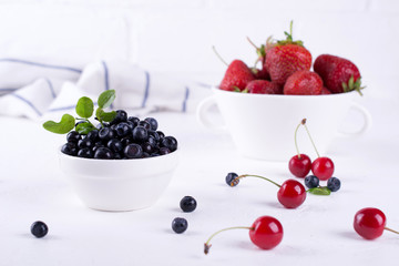 Fresh blueberriesand strawberry with green leaf  in a white bowl on a white background