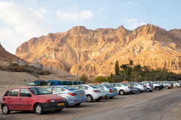 Obraz na płótnie Canvas Car park at Ein Gedi - National park and resort view of Negev desert mountain landscape in Israel. A small group of hikers walking on the path.