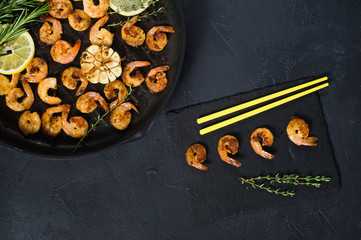 Pan with fried shrimps, fried garlic, rosemary. A stone plaque with shrimp sauce. Yellow Japanese chopsticks. Top view. Black background.