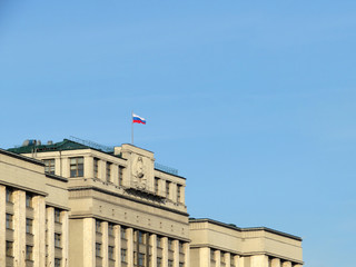 Russian flag on the Parliament building in Moscow against blue sky. Facade of State Duma of Russia...