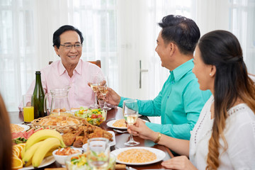 Obraz na płótnie Canvas Asian family having delicious meal and clinking with glasses at table on dinner spending time together
