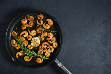 Pan with fried shrimps, fried garlic, rosemary. The view from the top. Black background. Space for text.