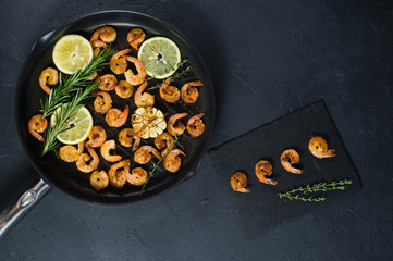 Pan with fried shrimps, fried garlic, rosemary. A stone plaque with shrimp sauce. The view from the top. Black background.