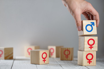 Hand putting a wooden cube with male icon on top of cubes with female logos