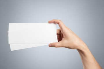 Obraz premium Hand holding two blank sheets of paper (tickets, flyers, invitations, coupons, banknotes, etc.), isolated on grey background