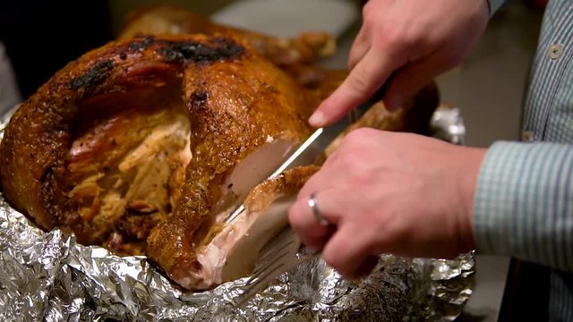 Slicing a turkey on a tinfoil with a knife then putting the piece of meat aside