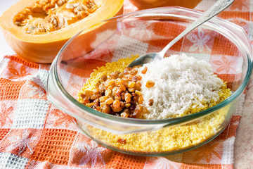 Fototapeta na wymiar Raw washed millet, rice and raisins in a glass pan in the process of cooking milk pumpkin porridge