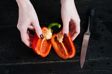chef cuts red bell pepper with a knife, top view, black background