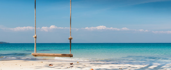 Wooden swing on the beach with tree,sea and blue sky of tropical island banner background and copy space.