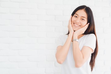 Happy smiling beautiful Asian woman gesturing with hands and showing two hands touch on her face in a white brick wall background.Concept of healthy and beauty lifestyle girl.