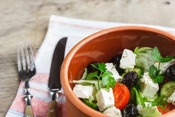 Vegetarian Greek salad with feta cheese, arugula, olives and cherry tomatoes and italian herbs in clay bowl