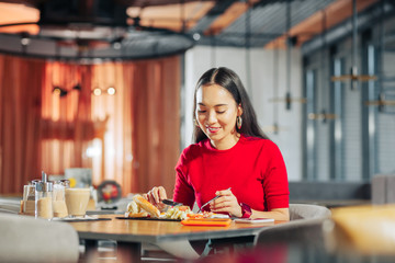 Appealing woman with long dark hair eating lunch in restaurant
