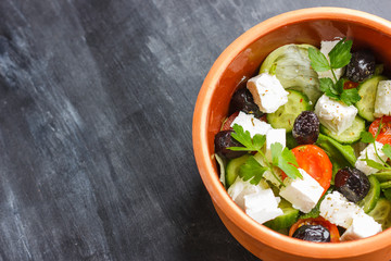 Vegetarian Greek salad with feta cheese, arugula, olives and cherry tomatoes and italian herbs in clay bowl