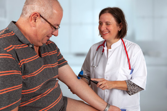 Smiling doctor is examining the biceps stretch reflex of her pati&euml;nt with a reflex hammer