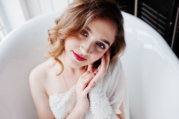 Pretty young curly gilrl in white dress sitting at bath.