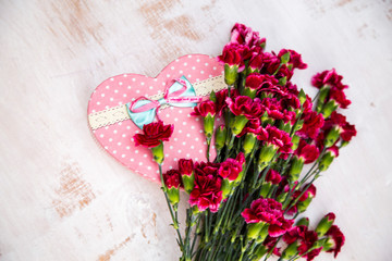 heart-shaped gift box with burgundy carnations lie on a light worn surface, flat lay