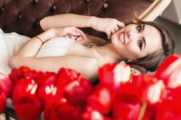 A beautiful young girl is lying on the sofa, and in front of her are red tulips. March 8 concept. Morning of the bride.