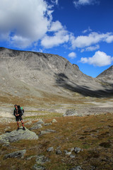 Young white Caucasian male tourist with backpack against the backdrop of mountains and clear blue sky with clouds in Karelia, Russia