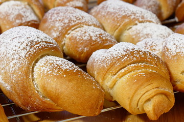Closeup of freshly baked homemade croissants sprinkled with powdered sugar left to cool down on a cookie rack. Love for baking at home.