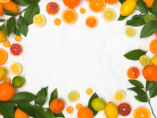 many different fresh citrus fruits on white crumpled paper background
