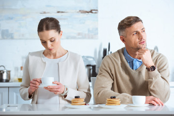 selective focus of adult couple sitting at table and ignoring each other during breakfast in morning