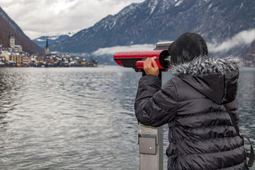 Fototapeta na wymiar A woman is looking through a telescope to the famous town of Hallstatt. Winter tourism in Austria.