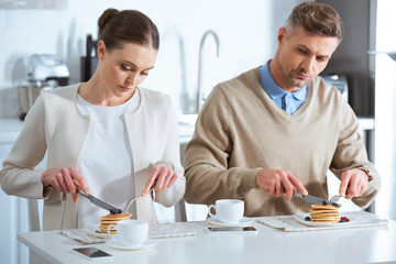 upset woman sitting at table and ignoring man during breakfast in morning