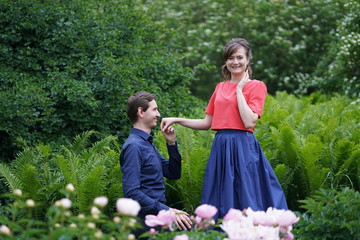 man on his knees makes an offer to be his wife to a woman in a summer blooming garden