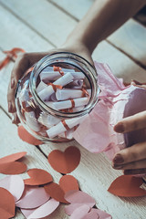 Lover's day. Hand opening glass jar or date Jar with desires. Red paper hearts at background.