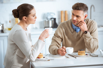 selective focus of dissatisfied adult couple sitting at table while having breakfast in morning