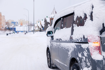 Closeup gray minibus dirty car covered with snow on city background. Side view. The concept snowy weather, snowfall, bad northern weather conditions, low battery, severe frost, travel big family
