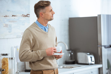 handsome man in casual clothes holding coffee cup in kitchen