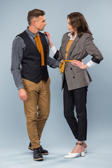 beautiful stylish couple in formal wear looking at each other and posing on grey background